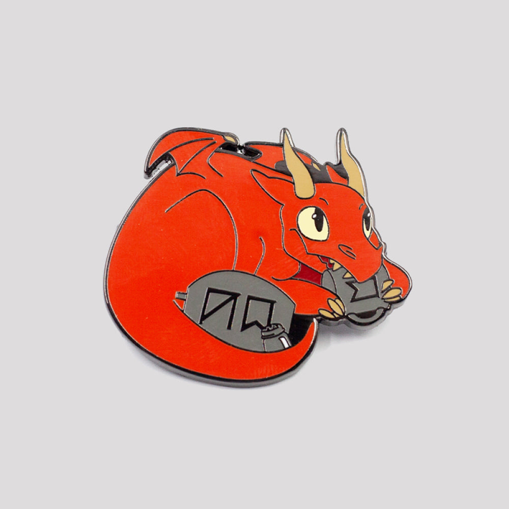 A vibrant red enamel Rune Eating Dragon pin by Unstable Games, with golden horns, clutching a gray book.