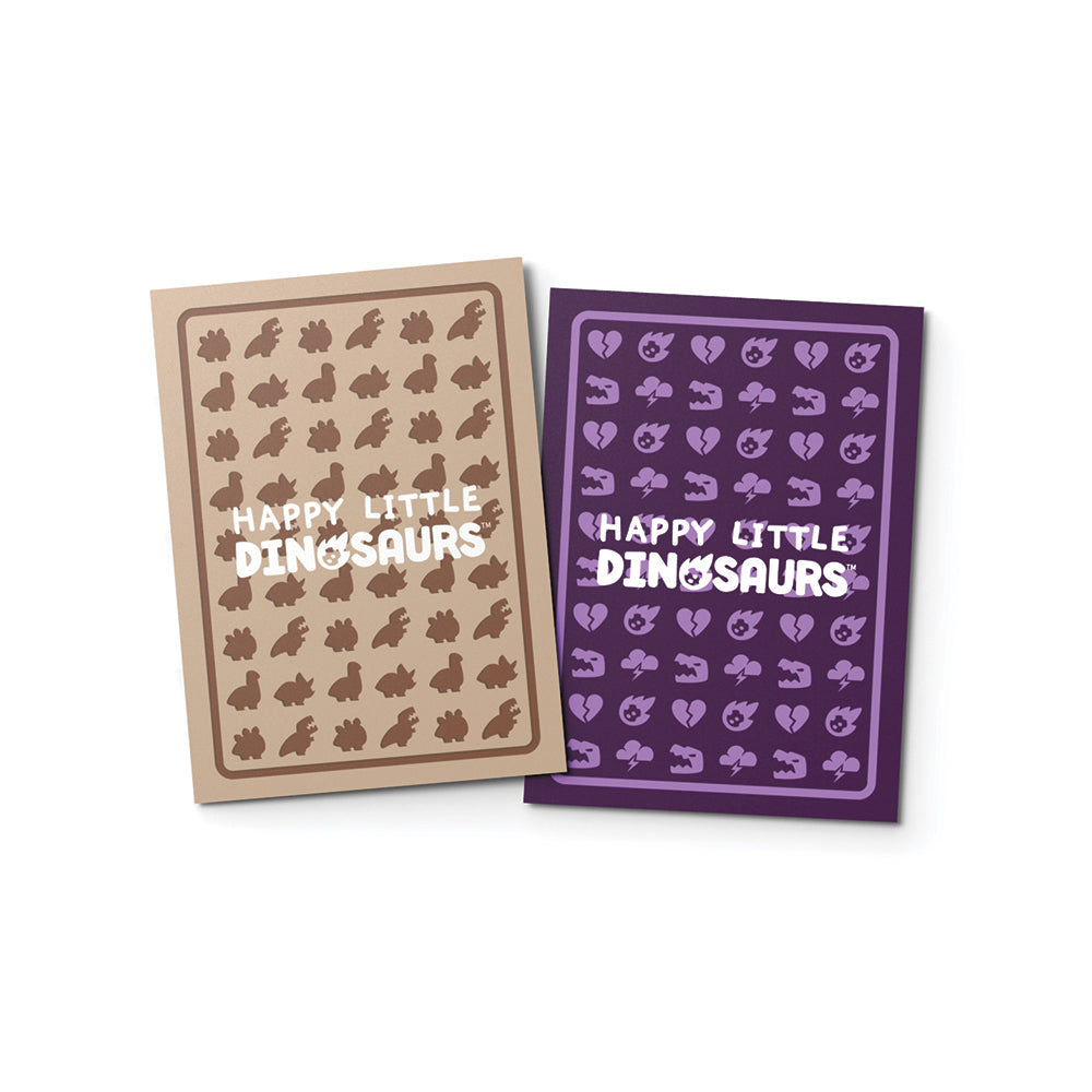 Two card decks labeled "Happy Little Dinosaurs," one in beige with brown dinosaur silhouettes, the other in purple with purple dinosaur silhouettes, both protected by Happy Little Dinosaurs: Standard Size Card Sleeves, displayed on Unstable Games.