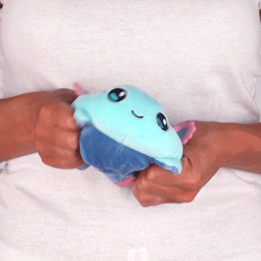 Person squeezing a Casting Shadows: Frill Lilypad & Frill the Regenerator Reversible Plushie from Unstable Games with a happy expression, showing its softness and squishiness.
