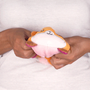 A person squeezes a Casting Shadows: Kit Gale & Kit the Turbulent Reversible Plushie from Unstable Games, resembling a cartoon fish, changing its shape, against a white background.