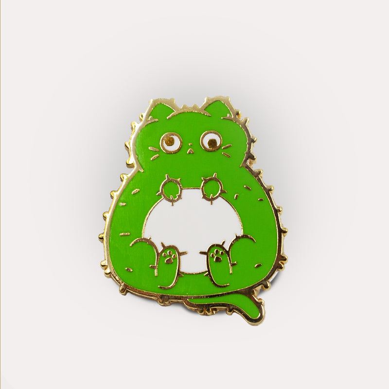 Cactus Cat Pin in the shape of a stylized dinosaur with bulging eyes and small spikes, isolated on a white background by Unstable Games.