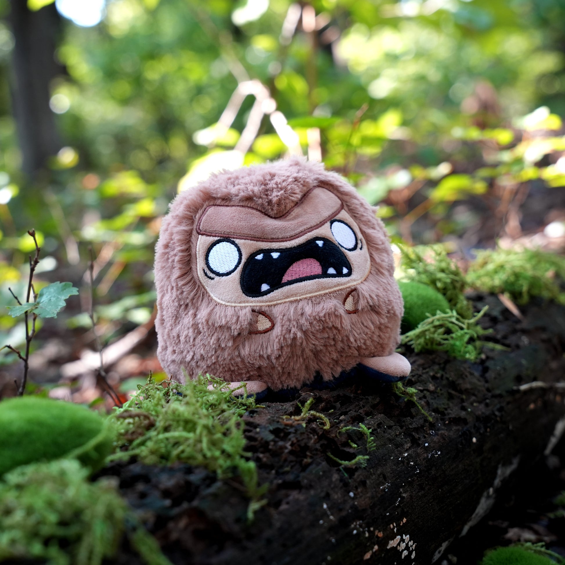 Twisted Cryptids: Bigfoot 4" Reversible Plushie angry side sitting on a mossy log in a forest