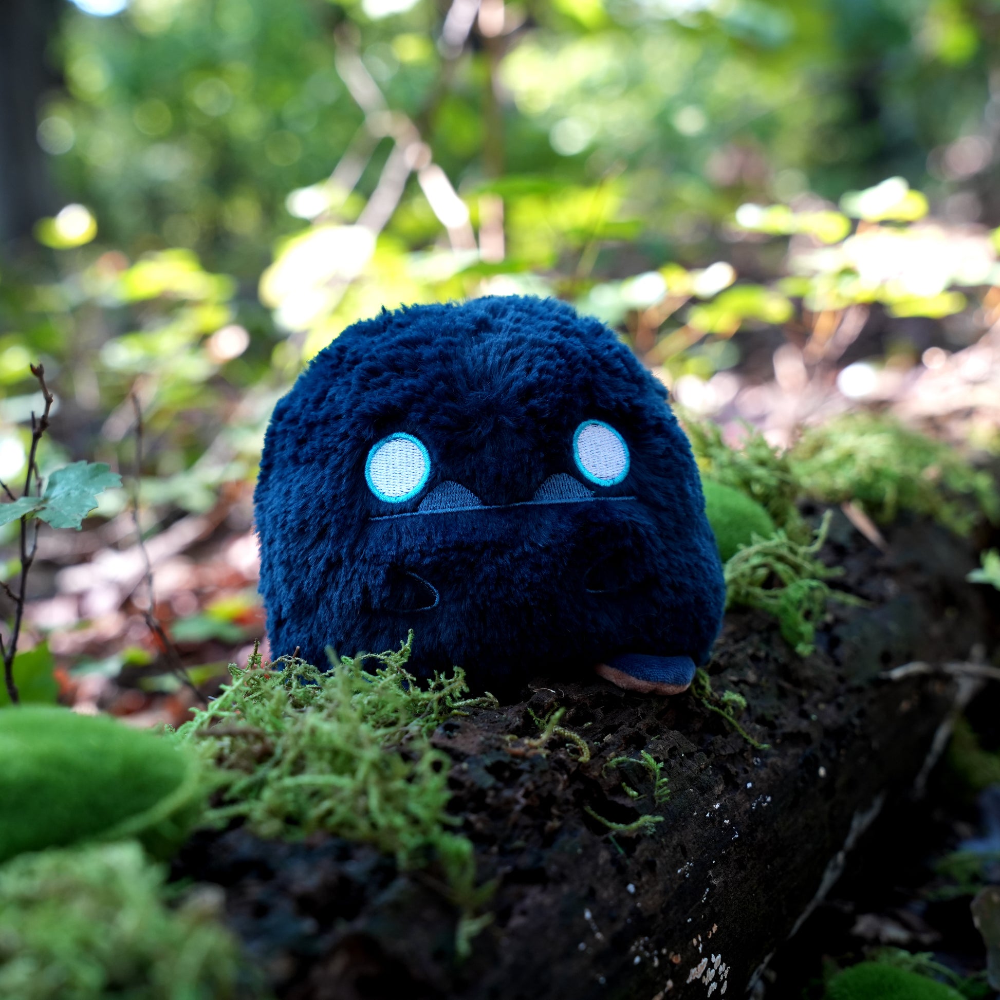 Twisted Cryptids: Bigfoot 4" Reversible Plushie neutral side sitting on a mossy log in a forest