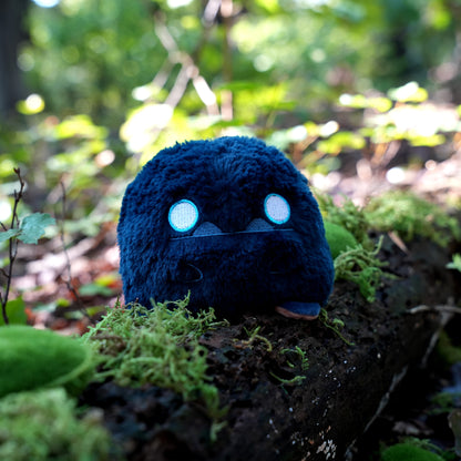 Twisted Cryptids: Bigfoot 4" Reversible Plushie neutral side sitting on a mossy log in a forest