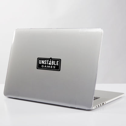 A laptop with a gray cover adorned with an Unstable Games sticker, positioned slightly open on a white surface.
