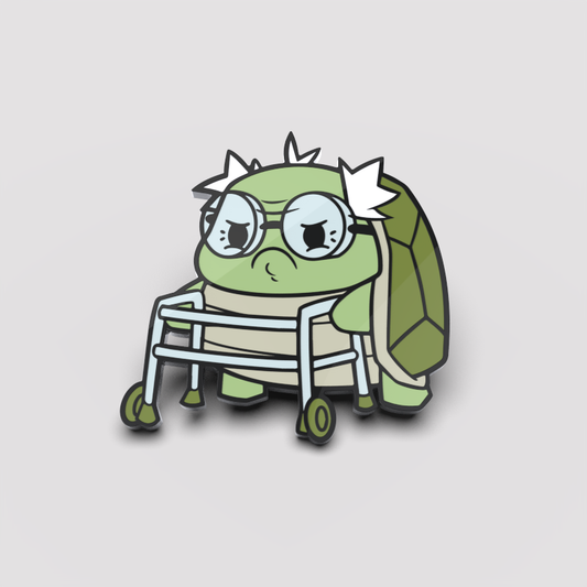 Cartoon of a sad green turtle with glasses, sitting in a wheelchair, against a light gray background, depicted on an Unstable Games Grumpy Grandpa Pin.