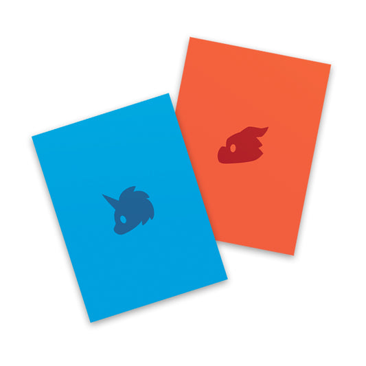 Two overlapping Tic Tac K.O. Dragons vs. Unicorns: Team Dragon + Team Unicorn card sleeves in blue and orange, each featuring a silhouette of a rocketship by Unstable Games.